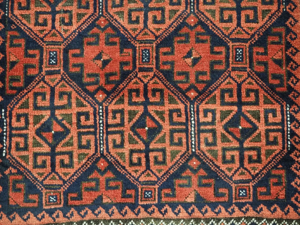 An antique hand-knotted wool rug featuring repeating geometric octagonal motifs in terracotta red and dark indigo blue. View XI