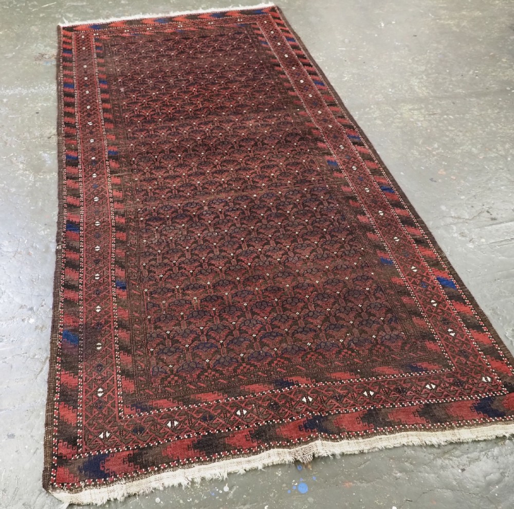 An antique hand-knotted Timuri Baluch wool rug featuring a dark red and brown field with a repeating small shrub design enclosed by geometric borders. View II