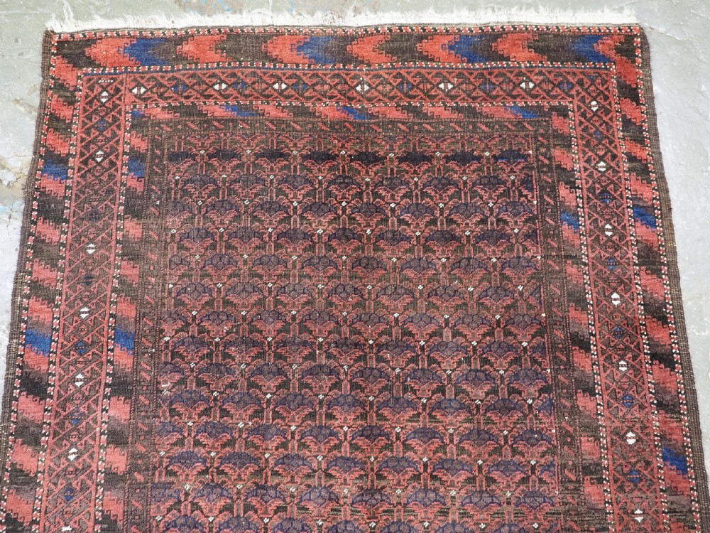 An antique hand-knotted Timuri Baluch wool rug featuring a dark red and brown field with a repeating small shrub design enclosed by geometric borders. View III