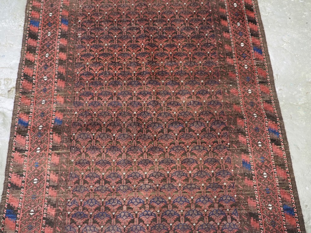 An antique hand-knotted Timuri Baluch wool rug featuring a dark red and brown field with a repeating small shrub design enclosed by geometric borders. View IV