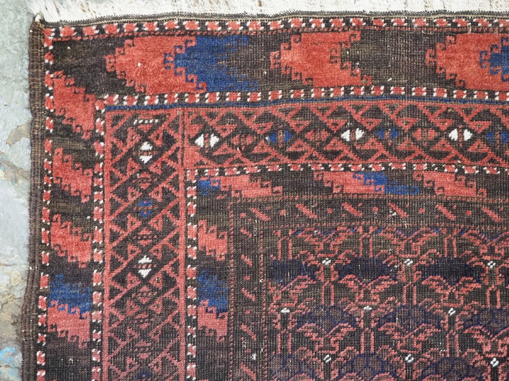 An antique hand-knotted Timuri Baluch wool rug featuring a dark red and brown field with a repeating small shrub design enclosed by geometric borders. View VI