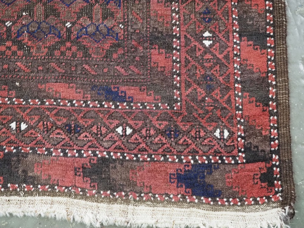 An antique hand-knotted Timuri Baluch wool rug featuring a dark red and brown field with a repeating small shrub design enclosed by geometric borders. View X