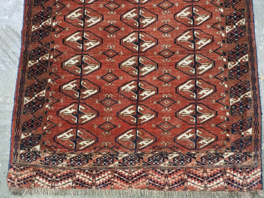 A hand-knotted antique Tekke Turkmen wool rug featuring repeating ovoid gul motifs set against a deep terracotta red background with geometric borders. View VI