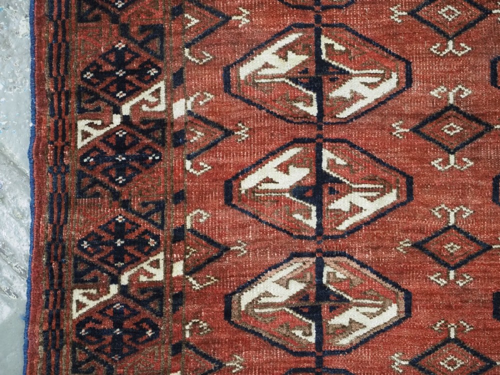 A hand-knotted antique Tekke Turkmen wool rug featuring repeating ovoid gul motifs set against a deep terracotta red background with geometric borders. View VII