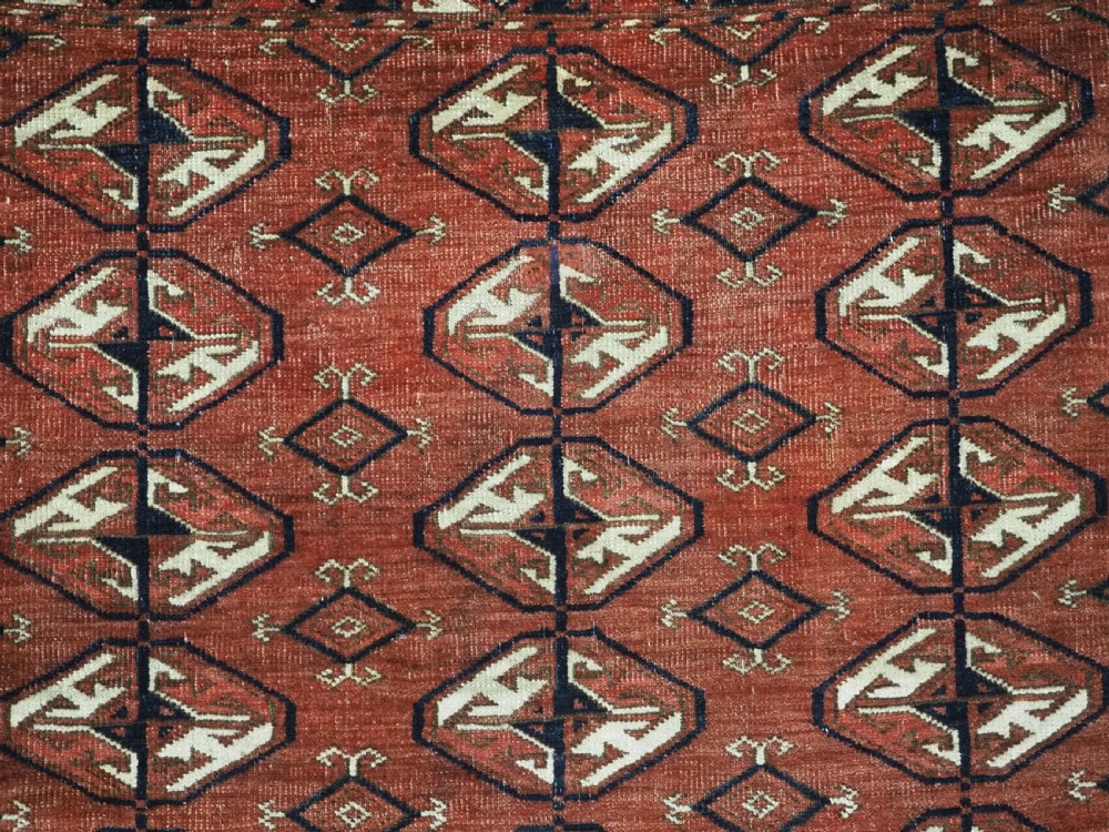 A hand-knotted antique Tekke Turkmen wool rug featuring repeating ovoid gul motifs set against a deep terracotta red background with geometric borders. View VIII