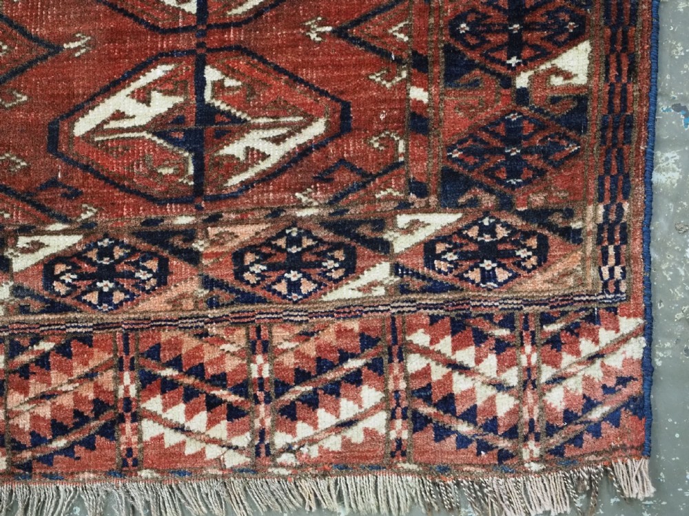 A hand-knotted antique Tekke Turkmen wool rug featuring repeating ovoid gul motifs set against a deep terracotta red background with geometric borders. View XI
