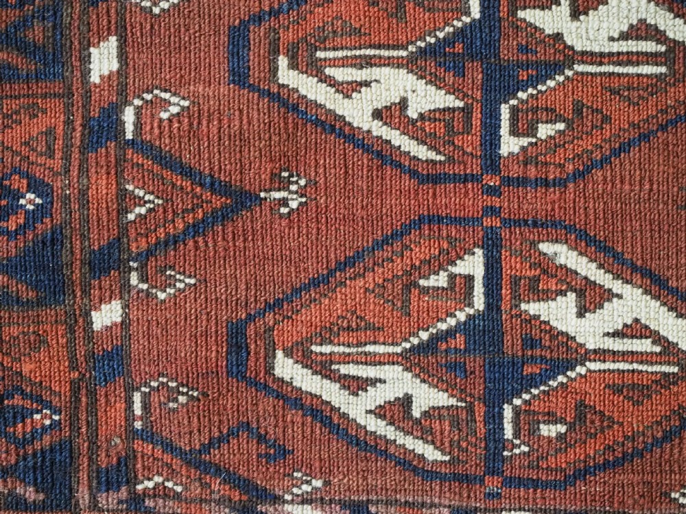 A hand-knotted antique Tekke Turkmen wool rug featuring repeating ovoid gul motifs set against a deep terracotta red background with geometric borders. View XII