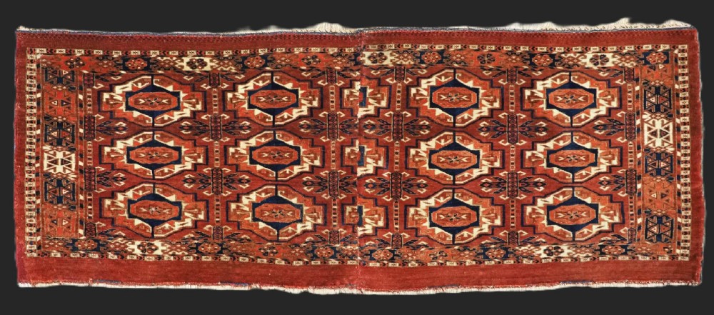 An antique Tekke Turkmen wool torba fragment featuring fifteen repeating octagonal geometric guls in terracotta red, cream, and navy blue.