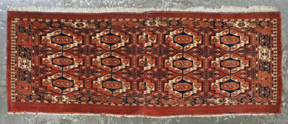 An antique Tekke Turkmen wool torba fragment featuring fifteen repeating octagonal geometric guls in terracotta red, cream, and navy blue. View II