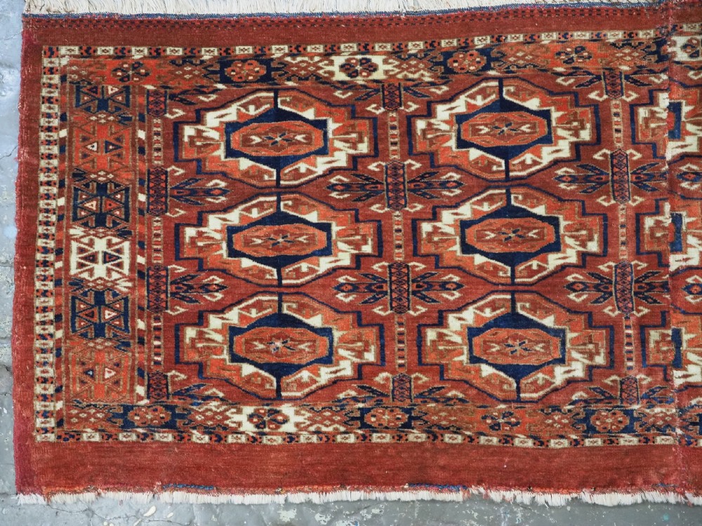 An antique Tekke Turkmen wool torba fragment featuring fifteen repeating octagonal geometric guls in terracotta red, cream, and navy blue. View III