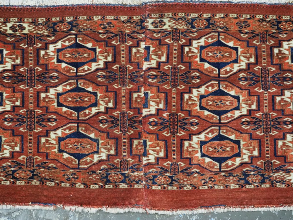 An antique Tekke Turkmen wool torba fragment featuring fifteen repeating octagonal geometric guls in terracotta red, cream, and navy blue. View IV