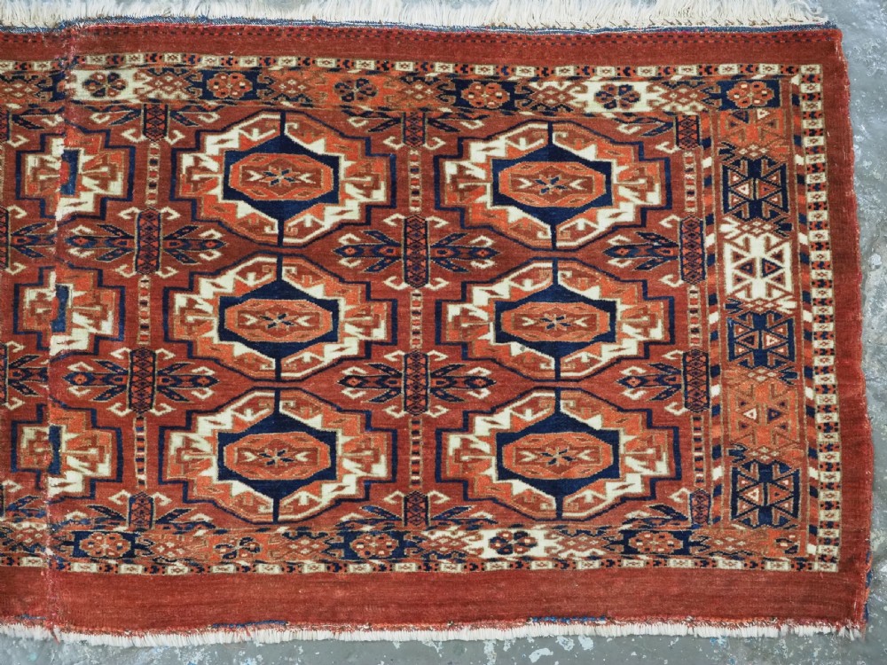 An antique Tekke Turkmen wool torba fragment featuring fifteen repeating octagonal geometric guls in terracotta red, cream, and navy blue. View V