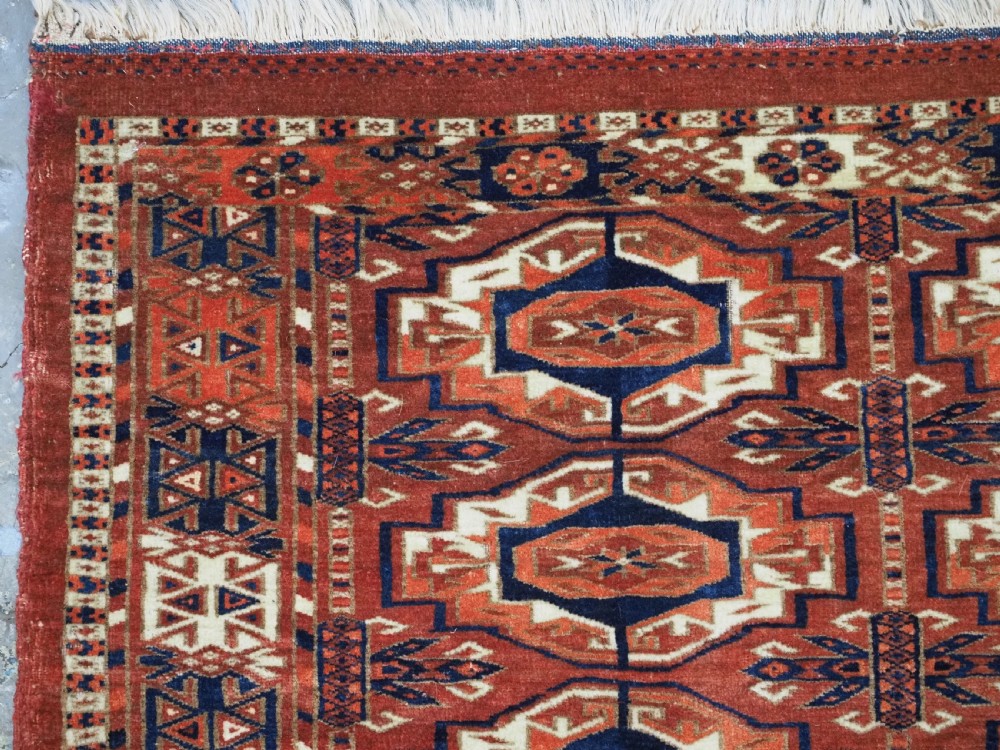An antique Tekke Turkmen wool torba fragment featuring fifteen repeating octagonal geometric guls in terracotta red, cream, and navy blue. View VI