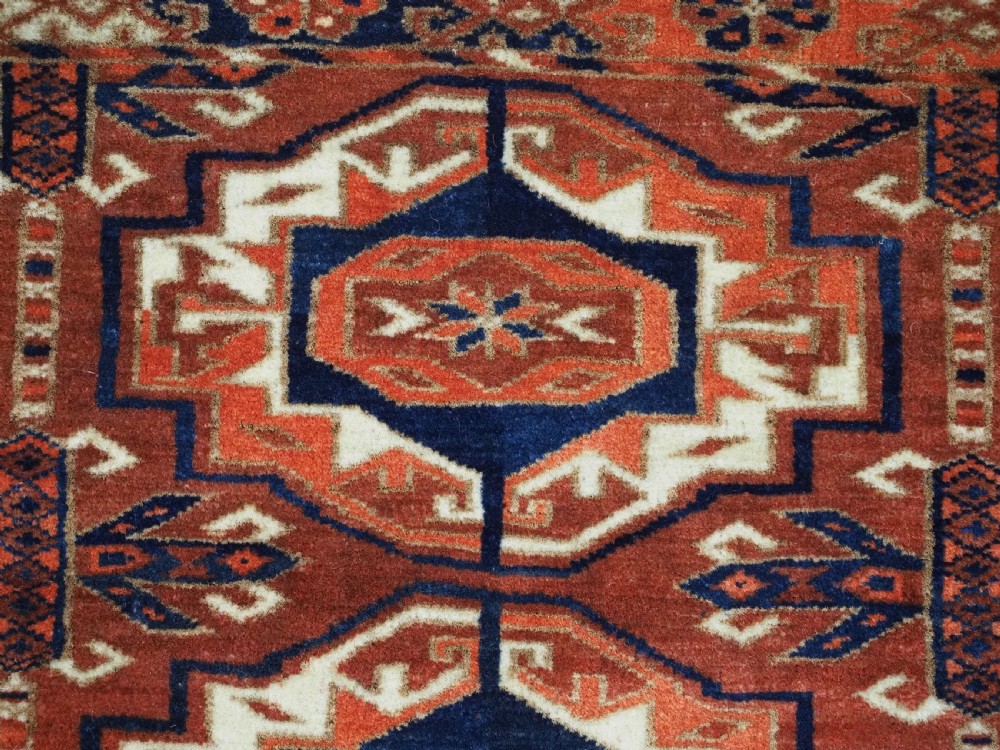 An antique Tekke Turkmen wool torba fragment featuring fifteen repeating octagonal geometric guls in terracotta red, cream, and navy blue. View VII