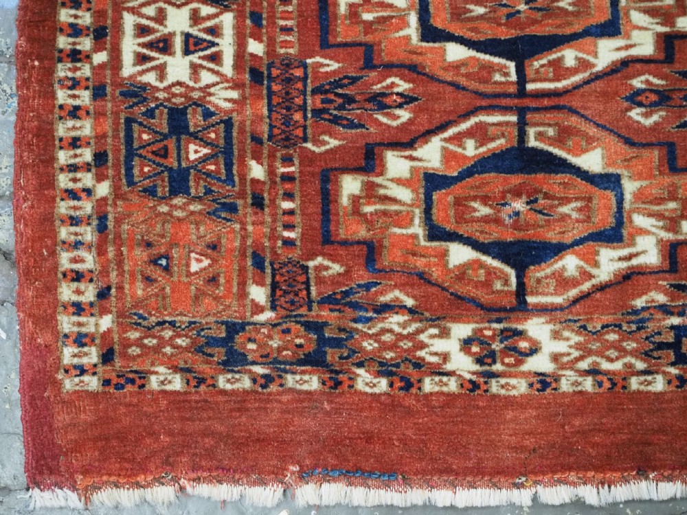 An antique Tekke Turkmen wool torba fragment featuring fifteen repeating octagonal geometric guls in terracotta red, cream, and navy blue. View VIII