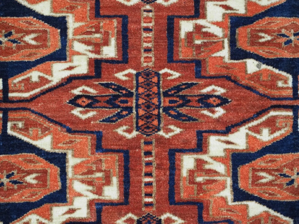 An antique Tekke Turkmen wool torba fragment featuring fifteen repeating octagonal geometric guls in terracotta red, cream, and navy blue. View IX