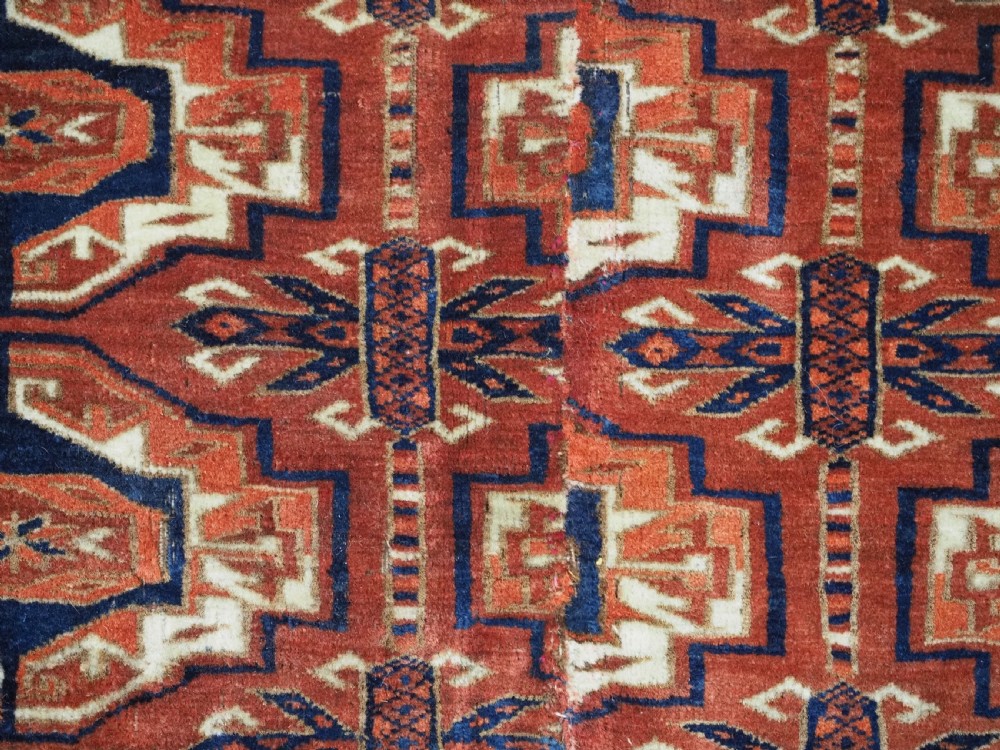 An antique Tekke Turkmen wool torba fragment featuring fifteen repeating octagonal geometric guls in terracotta red, cream, and navy blue. View X