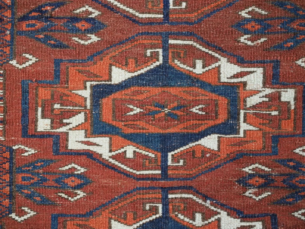 An antique Tekke Turkmen wool torba fragment featuring fifteen repeating octagonal geometric guls in terracotta red, cream, and navy blue. View XI