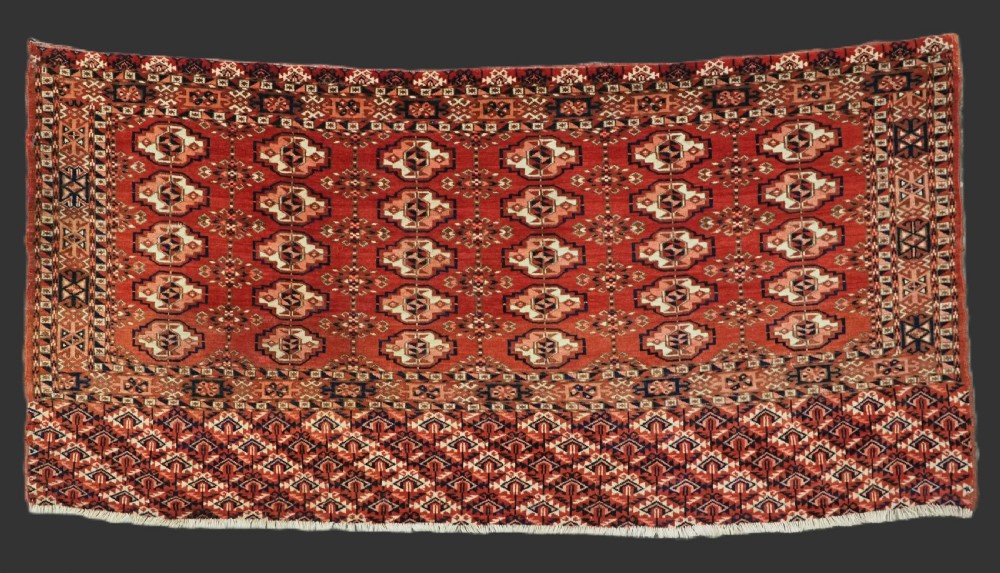 An antique Tekke Turkmen chuval woven textile face featuring thirty repeating octagonal guls on a deep red wool field with geometric borders and a decorated skirt.