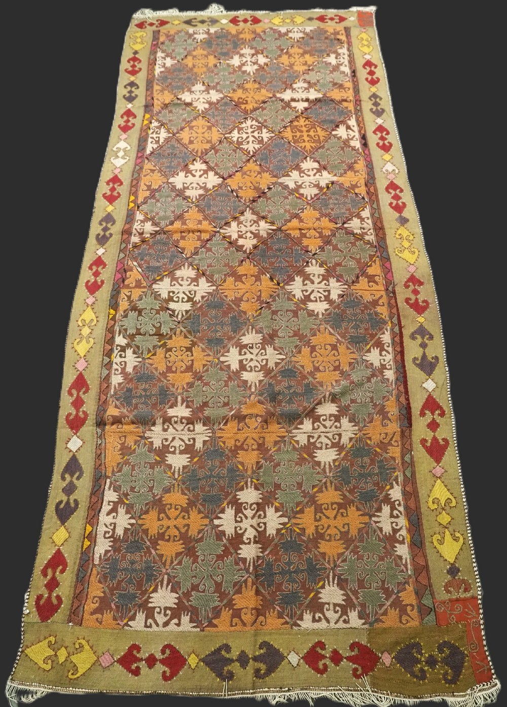 A long rectangular antique Uzbek handwoven wool suzani runner rug with a diamond lattice pattern and geometric border motifs in earth tones.
