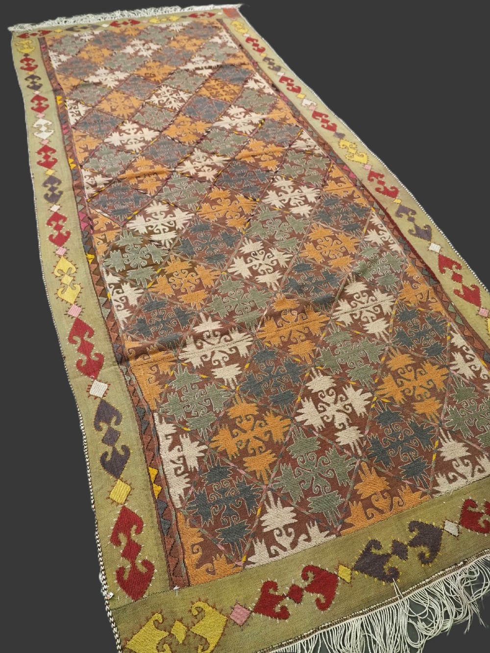 A long rectangular antique Uzbek handwoven wool suzani runner rug with a diamond lattice pattern and geometric border motifs in earth tones. View II