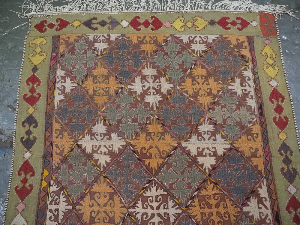 A long rectangular antique Uzbek handwoven wool suzani runner rug with a diamond lattice pattern and geometric border motifs in earth tones. View III