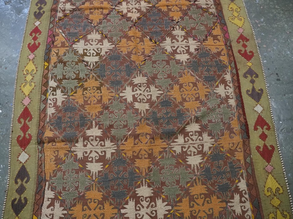 A long rectangular antique Uzbek handwoven wool suzani runner rug with a diamond lattice pattern and geometric border motifs in earth tones. View V