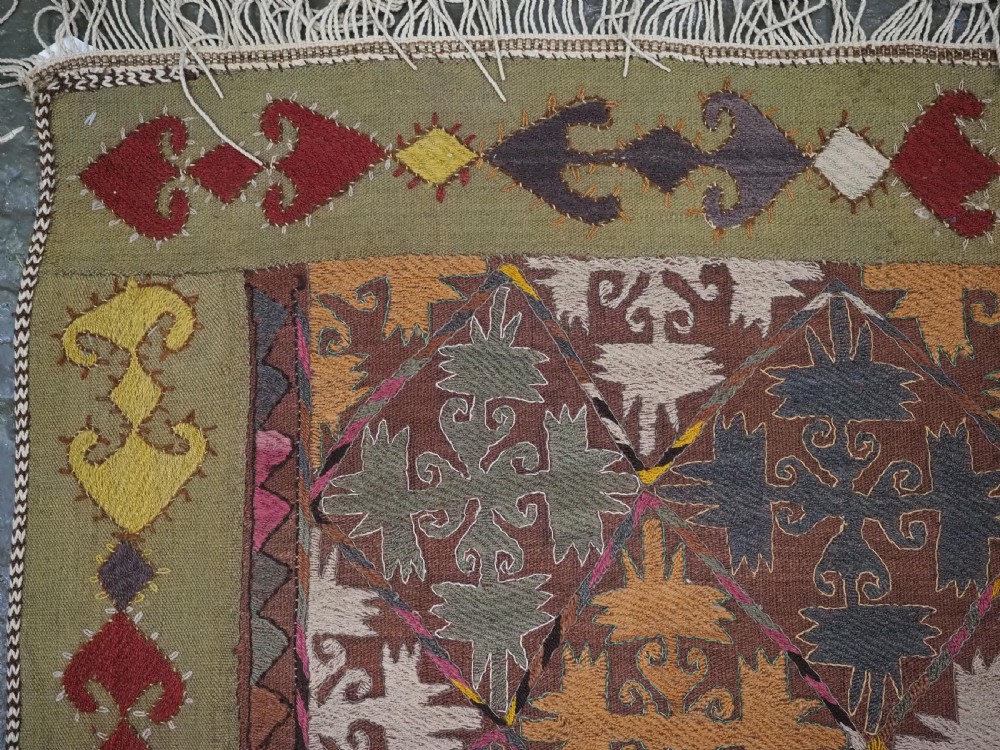 A long rectangular antique Uzbek handwoven wool suzani runner rug with a diamond lattice pattern and geometric border motifs in earth tones. View VII