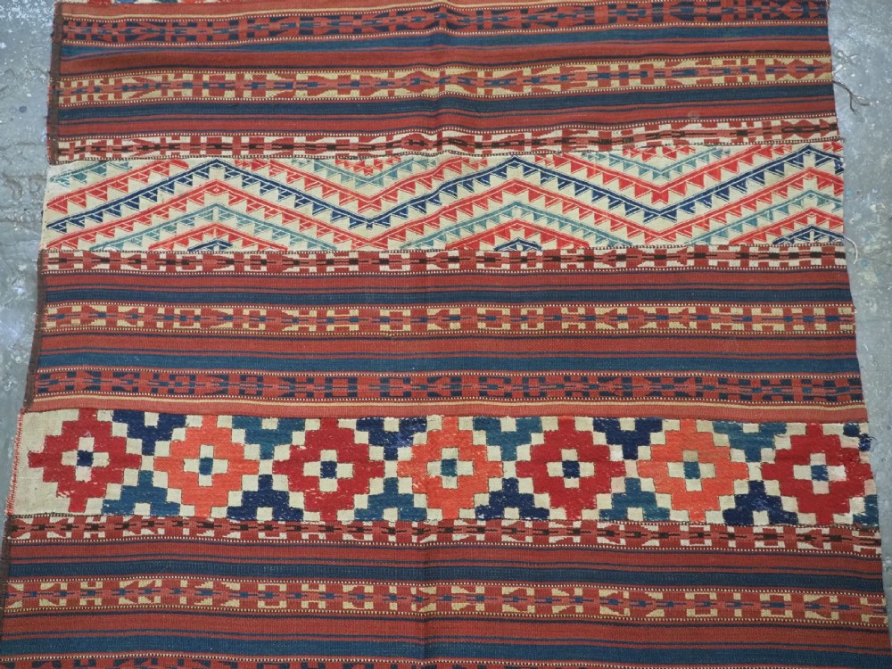 An antique central Asian kilim rug composed of thirteen vertical strips showing geometric diamond and stripe patterns in red, navy blue, and cream. View III
