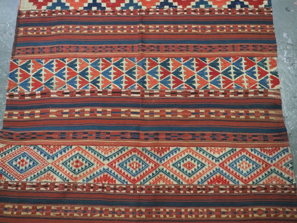An antique central Asian kilim rug composed of thirteen vertical strips showing geometric diamond and stripe patterns in red, navy blue, and cream. View IV