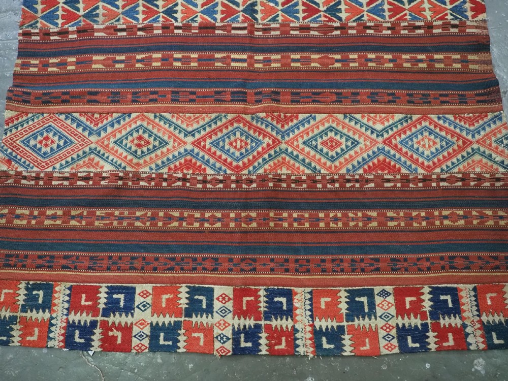An antique central Asian kilim rug composed of thirteen vertical strips showing geometric diamond and stripe patterns in red, navy blue, and cream. View V
