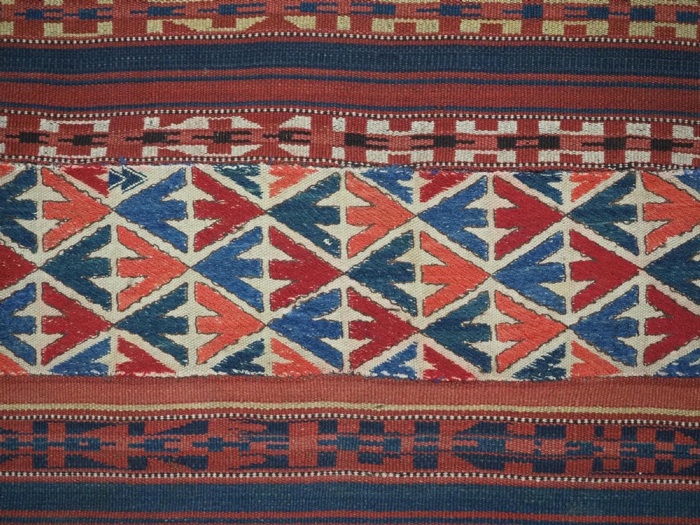 An antique central Asian kilim rug composed of thirteen vertical strips showing geometric diamond and stripe patterns in red, navy blue, and cream. View VII