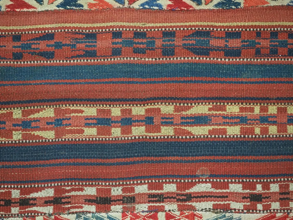An antique central Asian kilim rug composed of thirteen vertical strips showing geometric diamond and stripe patterns in red, navy blue, and cream. View VIII