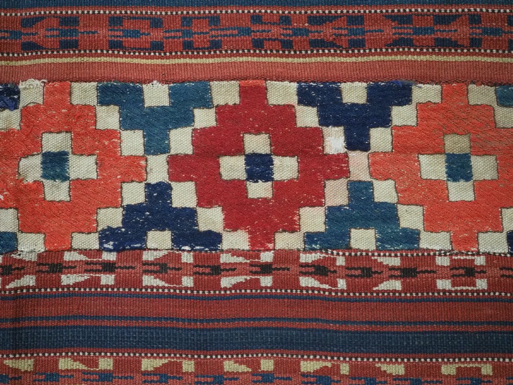 An antique central Asian kilim rug composed of thirteen vertical strips showing geometric diamond and stripe patterns in red, navy blue, and cream. View X