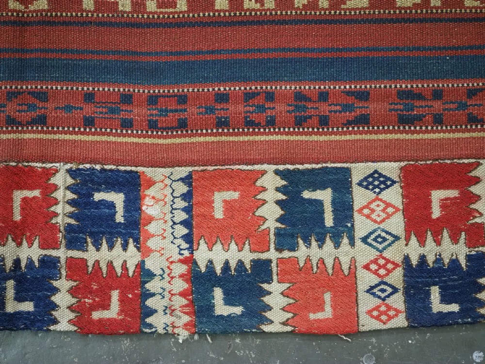 An antique central Asian kilim rug composed of thirteen vertical strips showing geometric diamond and stripe patterns in red, navy blue, and cream. View XIV