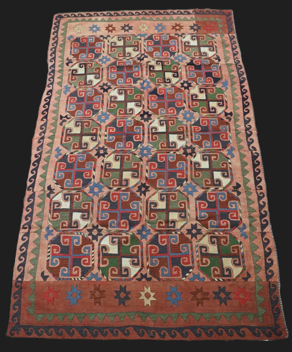 An antique flatweave rug composed of nine stitched vertical strips featuring repeating octagonal geometric motifs and star borders on a faded red background.