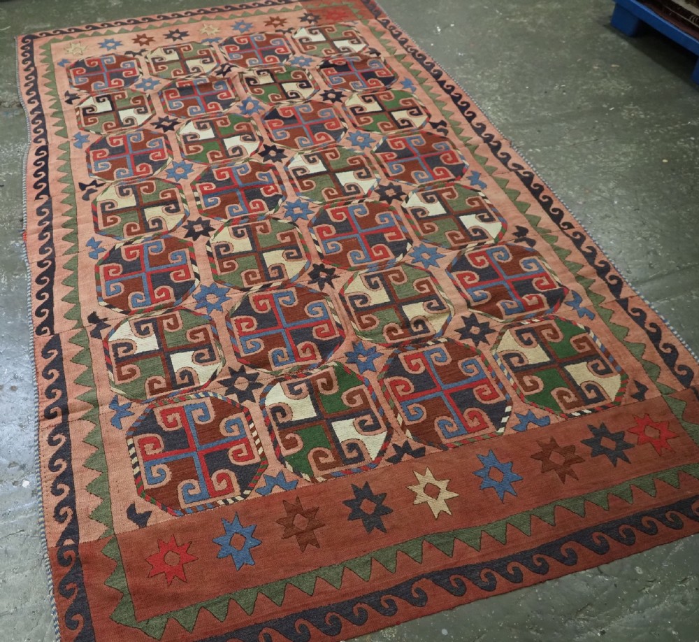An antique flatweave rug composed of nine stitched vertical strips featuring repeating octagonal geometric motifs and star borders on a faded red background. View II