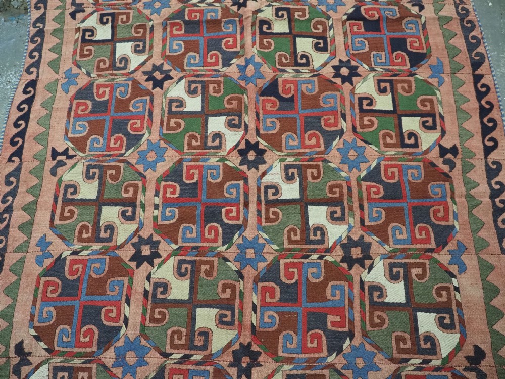 An antique flatweave rug composed of nine stitched vertical strips featuring repeating octagonal geometric motifs and star borders on a faded red background. View III