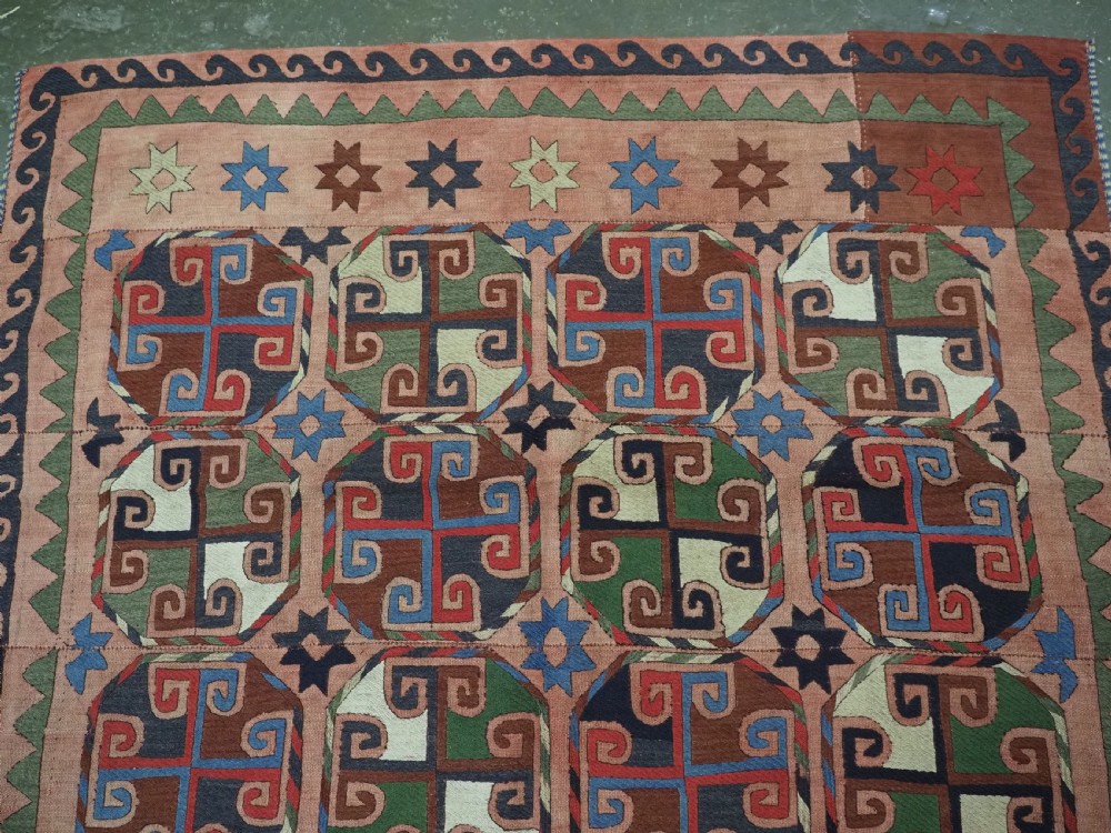 An antique flatweave rug composed of nine stitched vertical strips featuring repeating octagonal geometric motifs and star borders on a faded red background. View IV