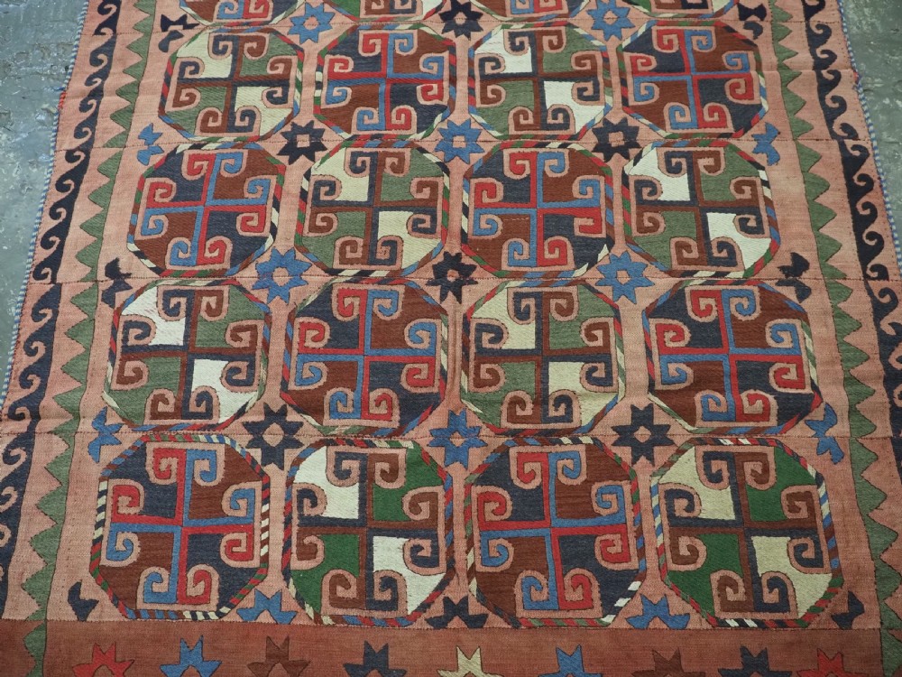 An antique flatweave rug composed of nine stitched vertical strips featuring repeating octagonal geometric motifs and star borders on a faded red background. View V