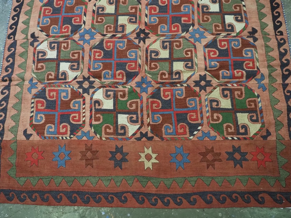 An antique flatweave rug composed of nine stitched vertical strips featuring repeating octagonal geometric motifs and star borders on a faded red background. View VI