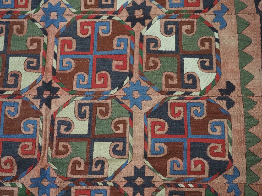 An antique flatweave rug composed of nine stitched vertical strips featuring repeating octagonal geometric motifs and star borders on a faded red background. View IX