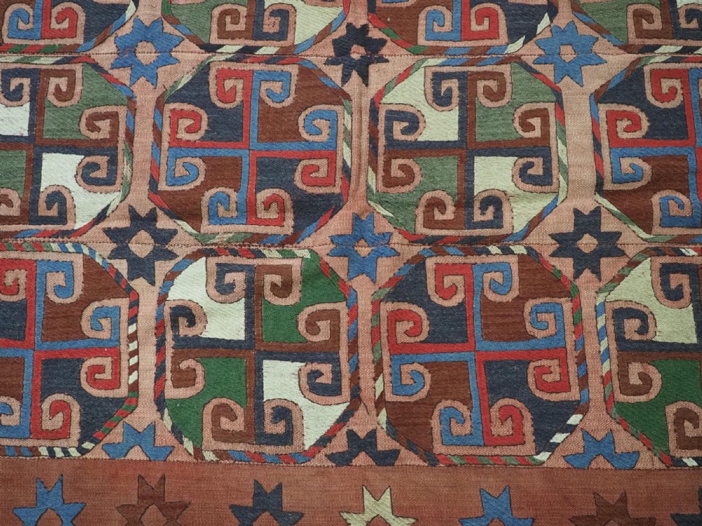 An antique flatweave rug composed of nine stitched vertical strips featuring repeating octagonal geometric motifs and star borders on a faded red background. View X