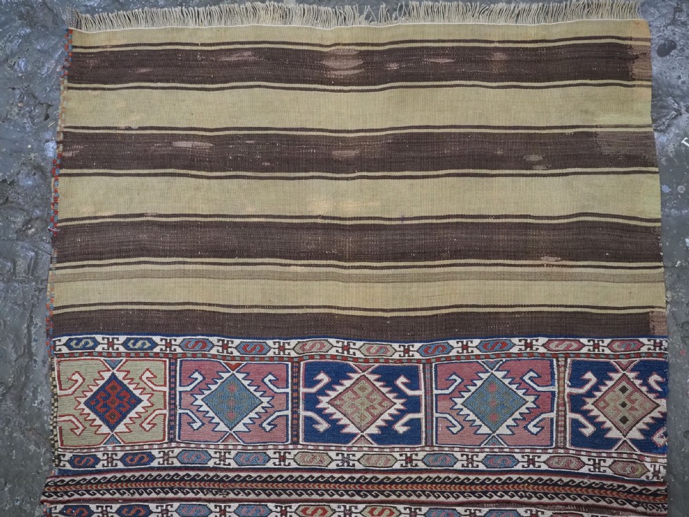 A flatwoven wool Caucasian kilim rug featuring horizontal brown and cream stripes alongside geometric diamond panels in indigo blue, terracotta, and green. View II