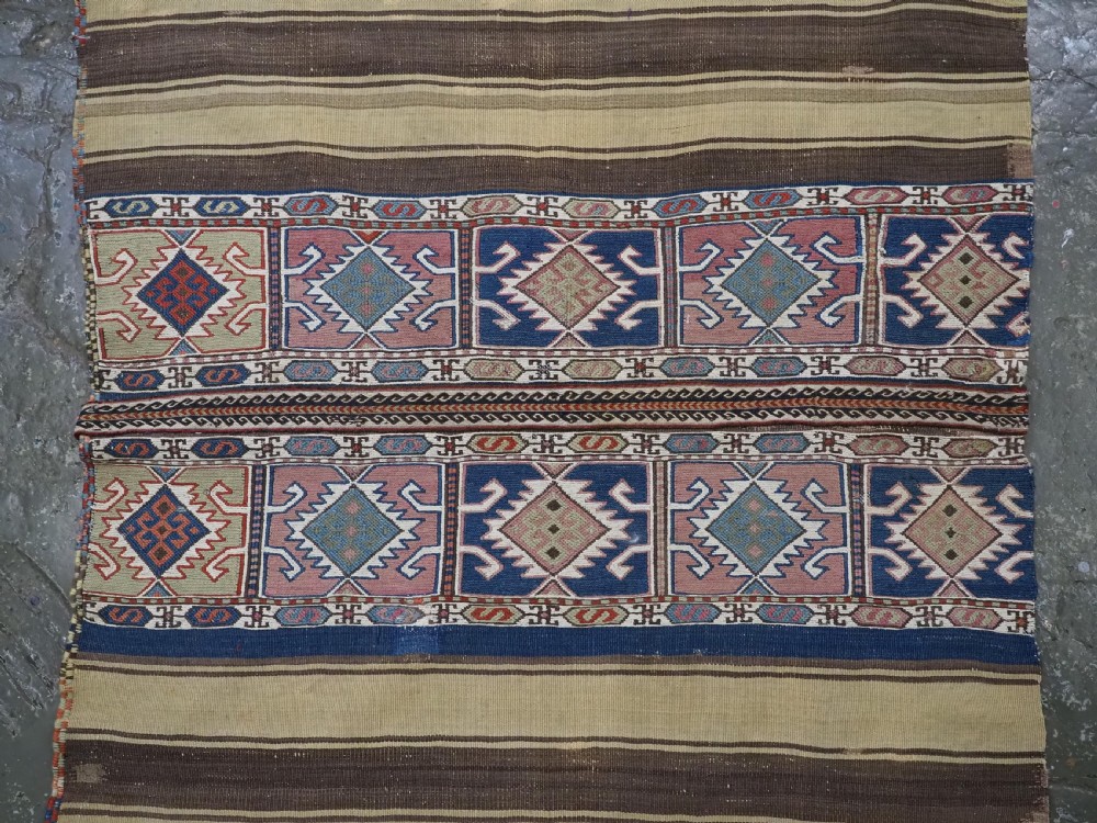A flatwoven wool Caucasian kilim rug featuring horizontal brown and cream stripes alongside geometric diamond panels in indigo blue, terracotta, and green. View III