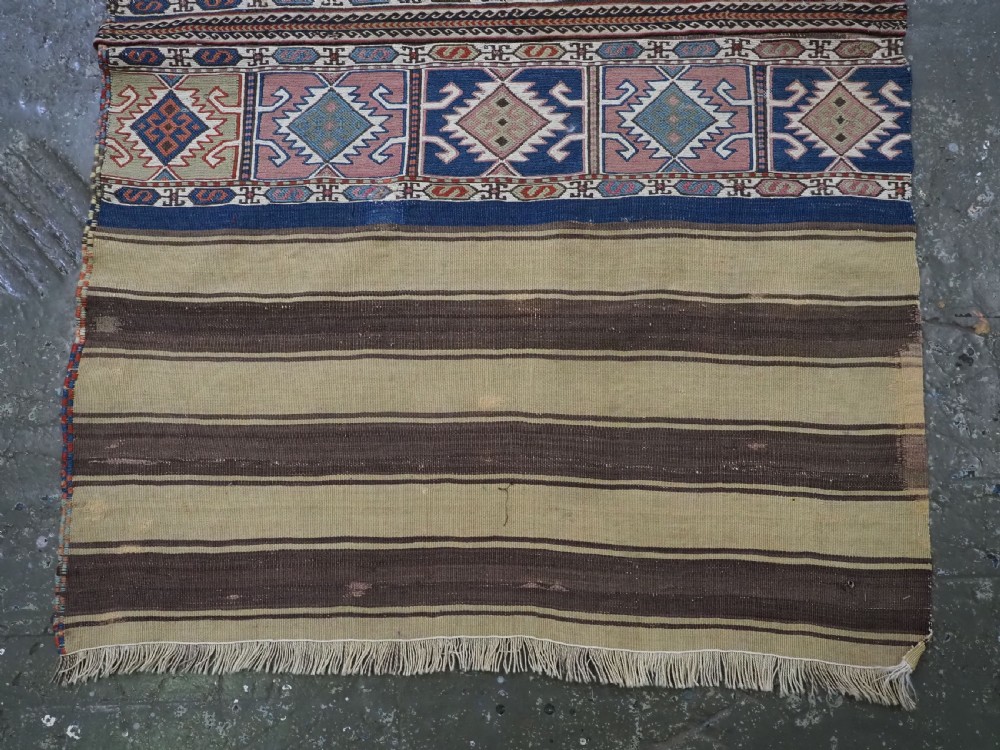 A flatwoven wool Caucasian kilim rug featuring horizontal brown and cream stripes alongside geometric diamond panels in indigo blue, terracotta, and green. View IV