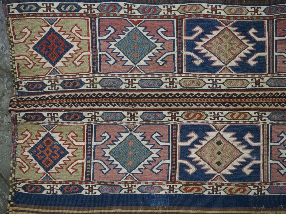 A flatwoven wool Caucasian kilim rug featuring horizontal brown and cream stripes alongside geometric diamond panels in indigo blue, terracotta, and green. View V