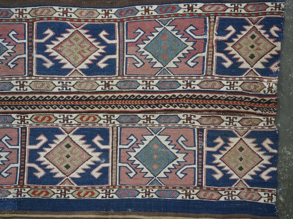 A flatwoven wool Caucasian kilim rug featuring horizontal brown and cream stripes alongside geometric diamond panels in indigo blue, terracotta, and green. View VI