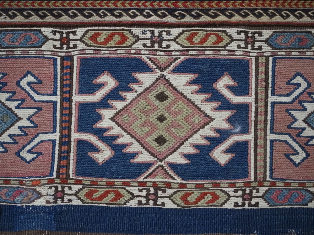 A flatwoven wool Caucasian kilim rug featuring horizontal brown and cream stripes alongside geometric diamond panels in indigo blue, terracotta, and green. View VII