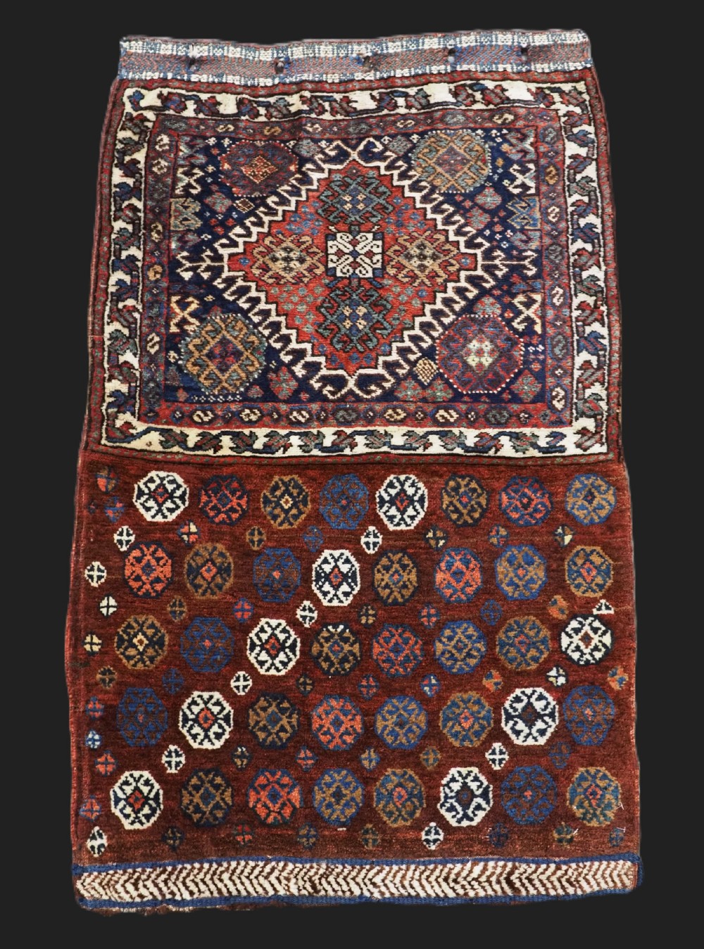 A late 19th-century South Persian hand-woven wool double saddle bag featuring geometric medallions, repeated guls, and stepped diamond patterns in shades of deep red, indigo blue, and ivory.